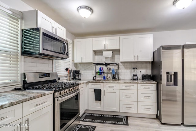 kitchen featuring appliances with stainless steel finishes, a sink, white cabinets, light stone counters, and decorative backsplash