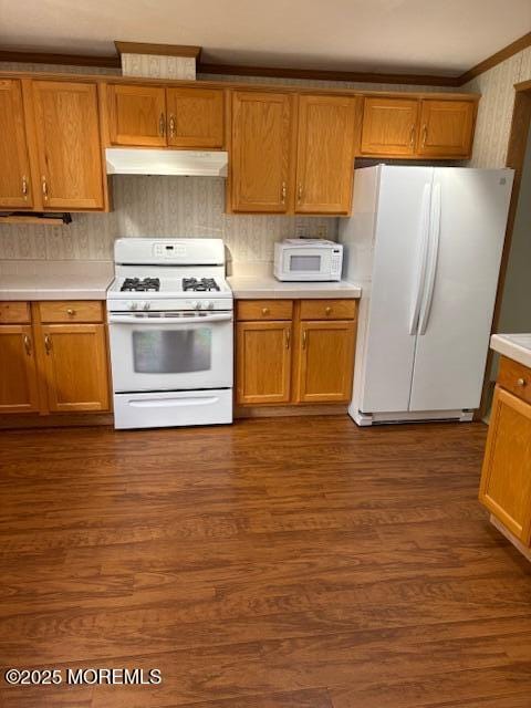 kitchen featuring white appliances, under cabinet range hood, light countertops, dark wood-type flooring, and ornamental molding