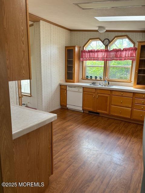 kitchen with white dishwasher, a sink, ornamental molding, wood finished floors, and brown cabinets
