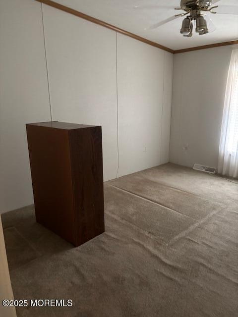 carpeted spare room with a ceiling fan and crown molding