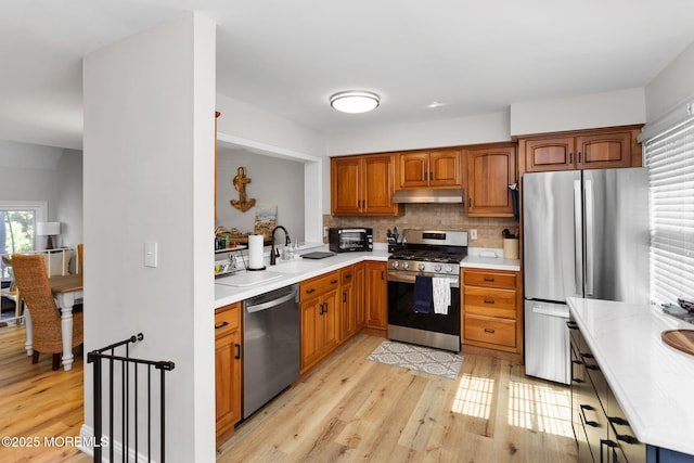 kitchen with appliances with stainless steel finishes, light wood-type flooring, light countertops, and under cabinet range hood
