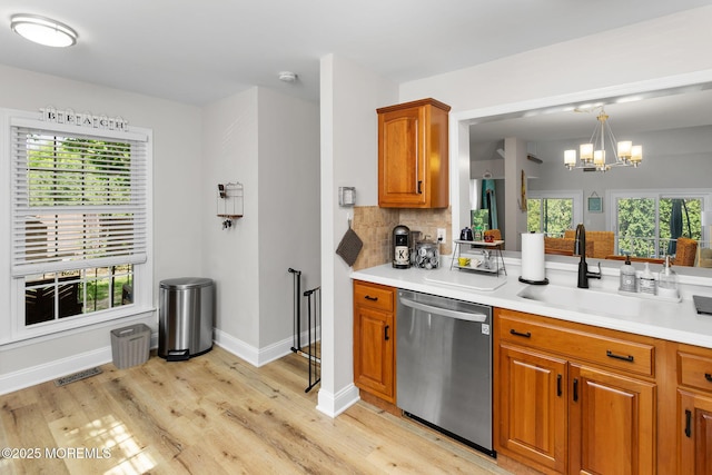 kitchen featuring stainless steel dishwasher, a chandelier, light wood-style floors, brown cabinetry, and a sink