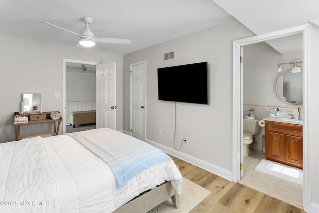 bedroom with a sink, light wood-style floors, ensuite bath, ceiling fan, and baseboards