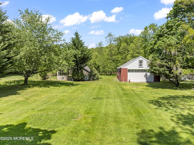 view of green lawn with a detached garage and an outbuilding
