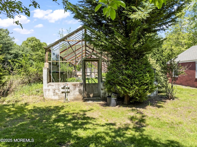 view of grassy yard with a greenhouse and an outbuilding