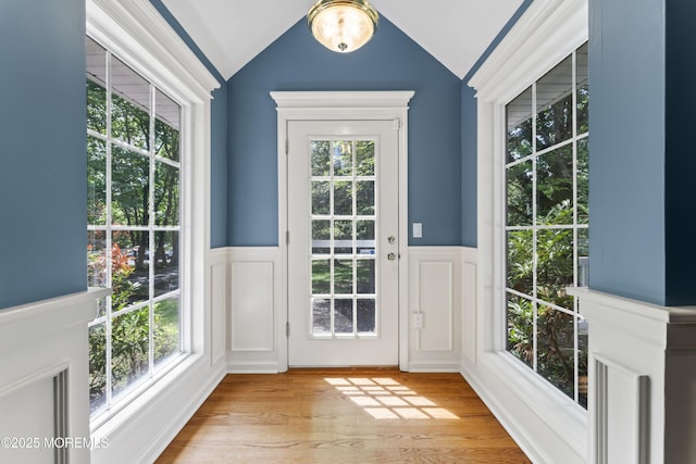 entryway with a wainscoted wall, a decorative wall, light wood finished floors, and vaulted ceiling