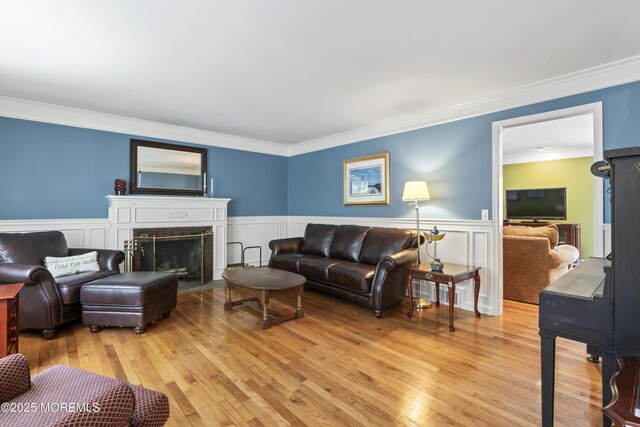 living room with light wood-style floors, ornamental molding, a fireplace with flush hearth, a wainscoted wall, and a decorative wall