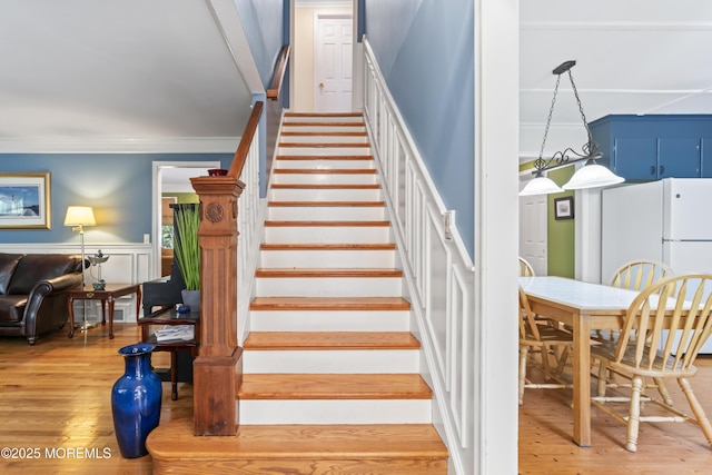 stairway featuring wood finished floors, ornamental molding, and wainscoting