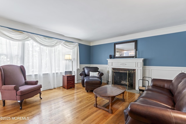 living room with a fireplace with flush hearth, ornamental molding, light wood-style floors, wainscoting, and a decorative wall