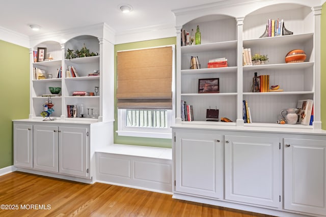 detailed view of wood finished floors, ornamental molding, and built in shelves