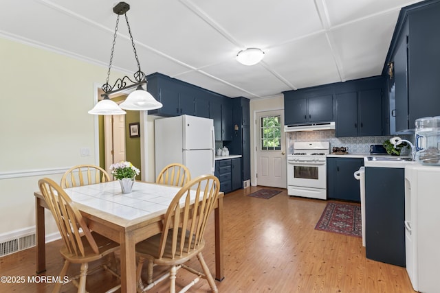kitchen with white appliances, under cabinet range hood, blue cabinetry, light countertops, and light wood-style floors