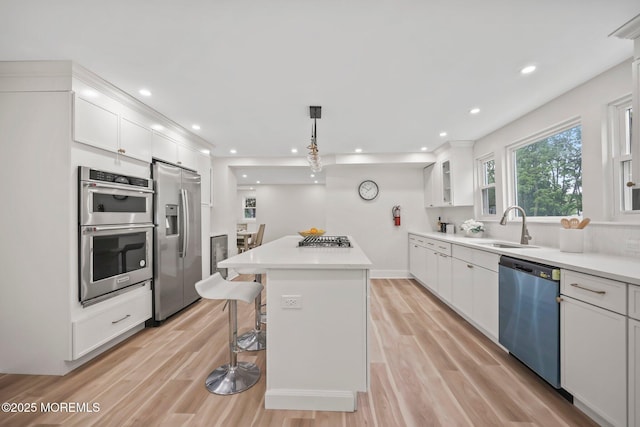 kitchen with appliances with stainless steel finishes, white cabinetry, a kitchen island, a sink, and light wood-type flooring