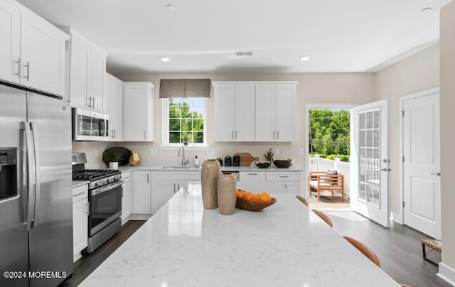 kitchen featuring stainless steel appliances, light stone countertops, white cabinets, a sink, and recessed lighting