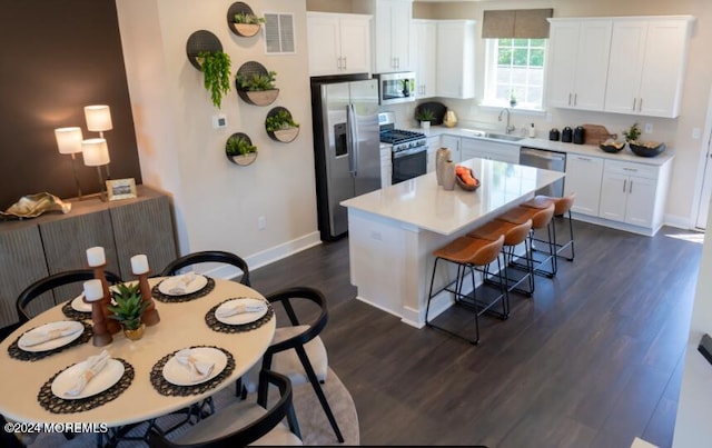 kitchen with stainless steel appliances, a sink, dark wood-style floors, a kitchen breakfast bar, and light countertops