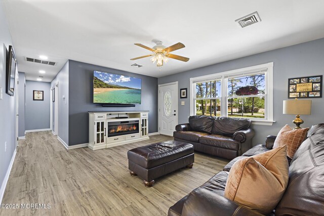 living room with light wood finished floors, ceiling fan, baseboards, and a glass covered fireplace