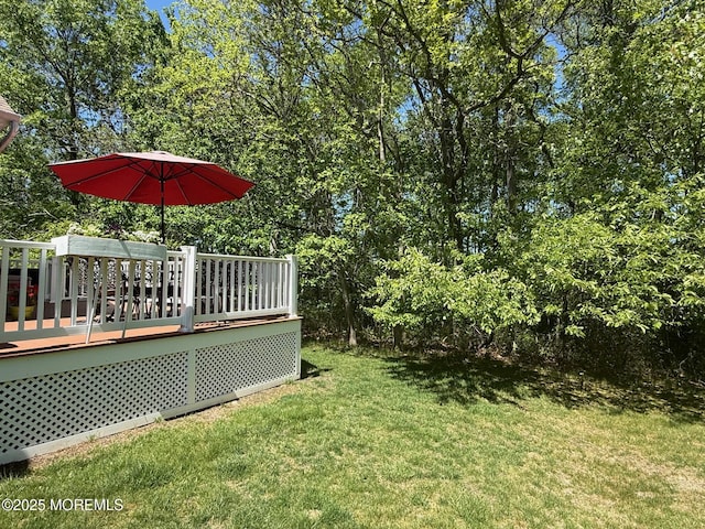 view of grassy yard featuring a wooden deck and view of scattered trees