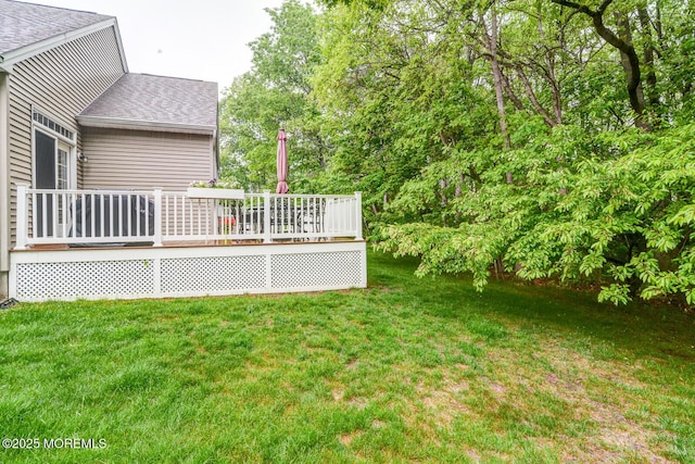 view of grassy yard featuring a deck and view of wooded area