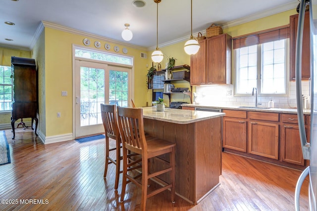 kitchen with a sink, light wood-style floors, ornamental molding, a kitchen island, and backsplash