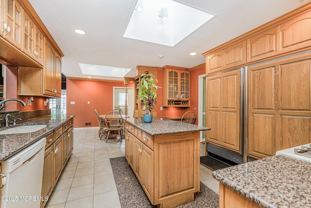 kitchen with white dishwasher, a sink, a skylight, a kitchen island, and glass insert cabinets