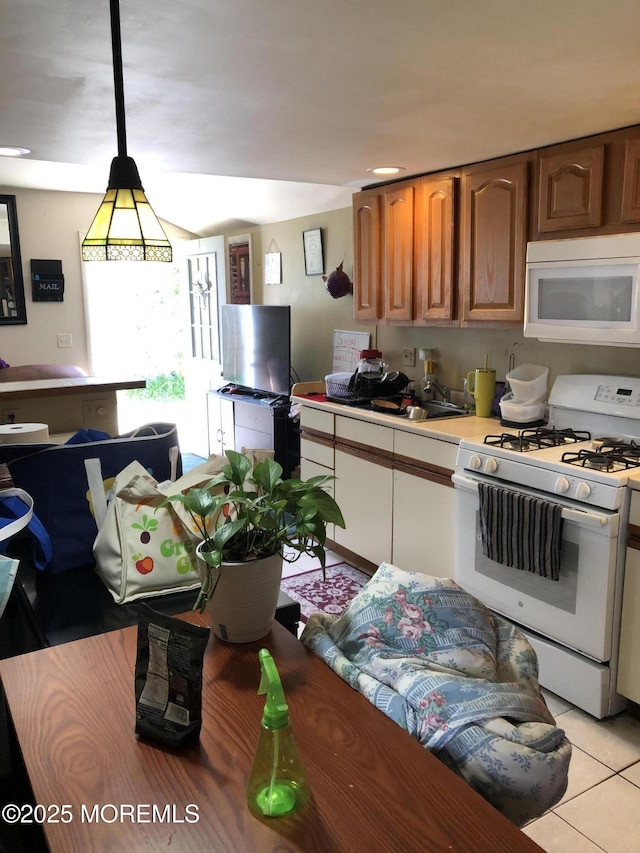 kitchen featuring white appliances, a sink, light countertops, light tile patterned flooring, and hanging light fixtures