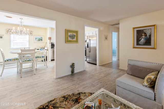 living area featuring a chandelier, light wood-style flooring, and baseboards