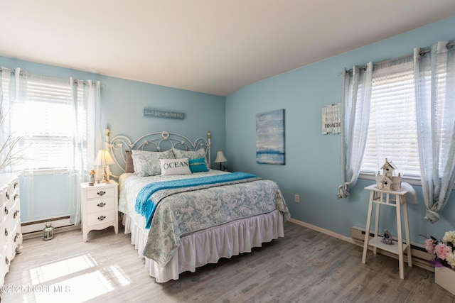 bedroom with wood finished floors, a baseboard heating unit, and baseboards