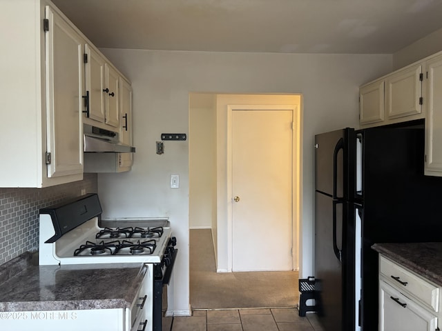 kitchen with gas range oven, under cabinet range hood, dark countertops, carpet flooring, and freestanding refrigerator