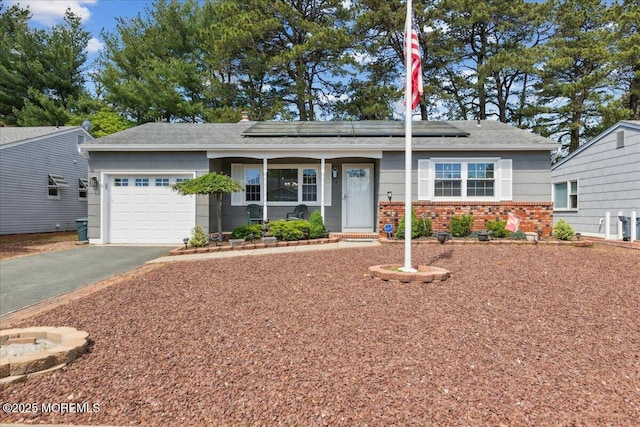 ranch-style house featuring asphalt driveway, an attached garage, brick siding, and solar panels