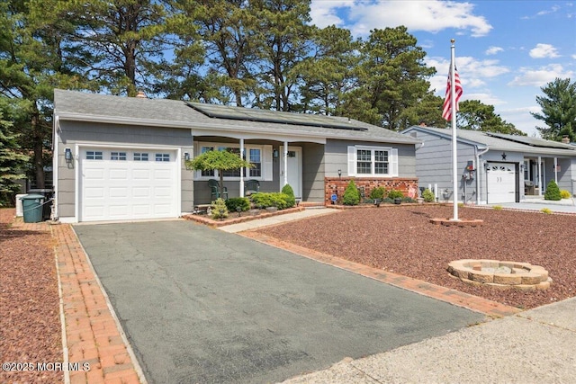 ranch-style house with a garage, driveway, roof mounted solar panels, covered porch, and a shingled roof