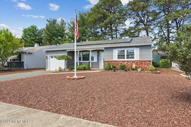 ranch-style house with driveway, a garage, solar panels, and brick siding