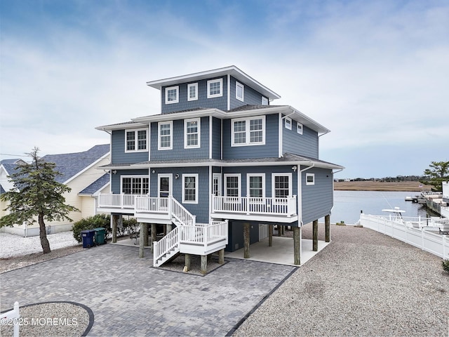 back of house featuring a carport, decorative driveway, a water view, stairway, and covered porch