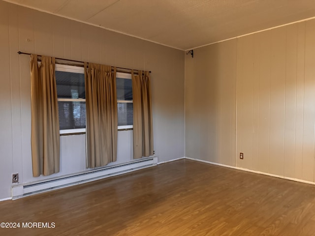 unfurnished room featuring a baseboard heating unit, wood finished floors, and baseboards