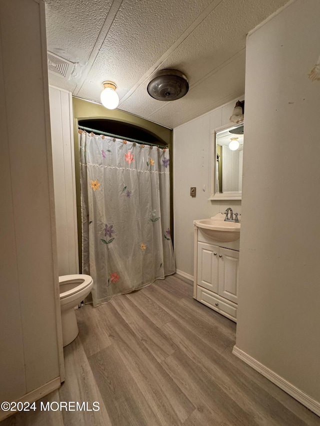 bathroom featuring wood finished floors, toilet, vanity, a textured ceiling, and baseboards