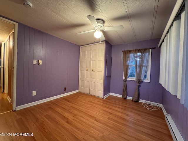 unfurnished bedroom with wood finished floors, a baseboard radiator, a textured ceiling, baseboards, and a ceiling fan