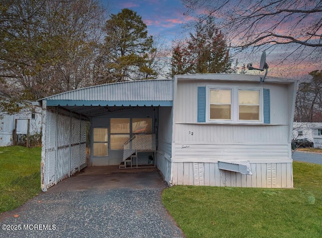 outdoor structure at dusk featuring asphalt driveway, a yard, and an attached carport