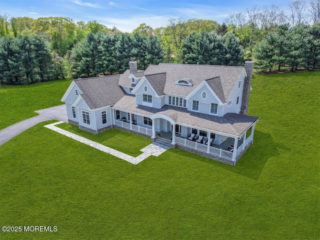 view of front of property featuring covered porch, a chimney, a front yard, and driveway