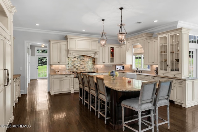 kitchen featuring cream cabinets, a center island, a sink, dark wood-style flooring, and ornamental molding