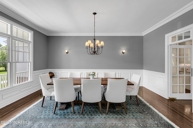 dining area with plenty of natural light, wood finished floors, a chandelier, crown molding, and a wainscoted wall