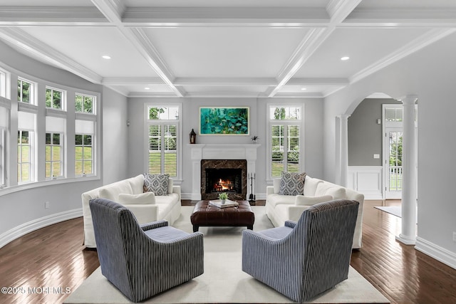 living area with ornate columns, arched walkways, wood finished floors, a high end fireplace, and coffered ceiling