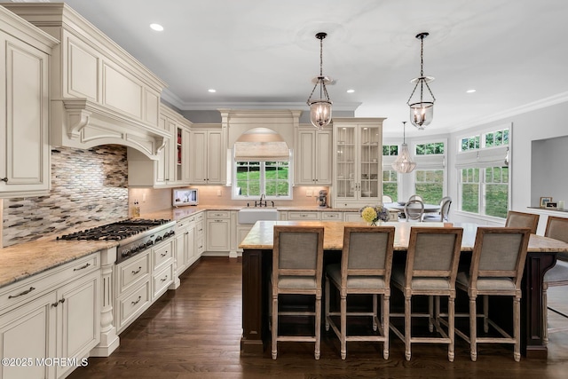 kitchen with cream cabinets, a sink, stainless steel gas stovetop, plenty of natural light, and ornamental molding