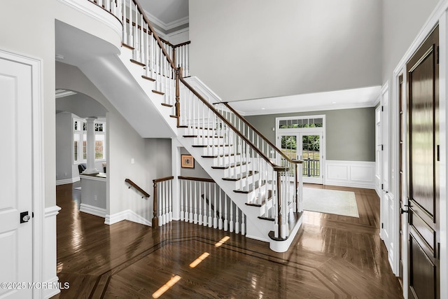 staircase featuring a towering ceiling, arched walkways, french doors, ornate columns, and crown molding