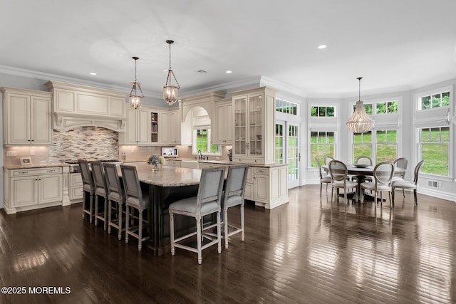 kitchen with cream cabinets, a sink, glass insert cabinets, ornamental molding, and recessed lighting