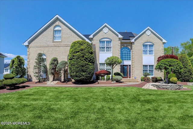 view of front of property featuring a front yard, roof mounted solar panels, and brick siding