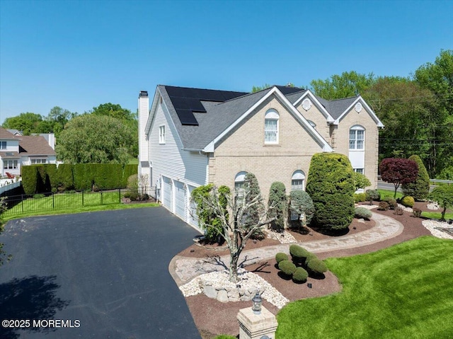 view of front of home featuring asphalt driveway, a garage, a chimney, roof mounted solar panels, and brick siding