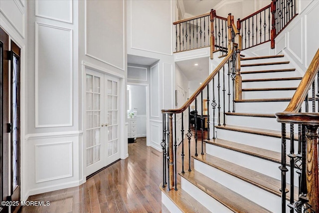 stairs featuring a decorative wall, a high ceiling, french doors, and wood finished floors