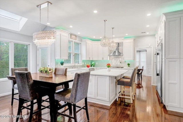 kitchen featuring a chandelier, a skylight, wall chimney range hood, appliances with stainless steel finishes, and light countertops
