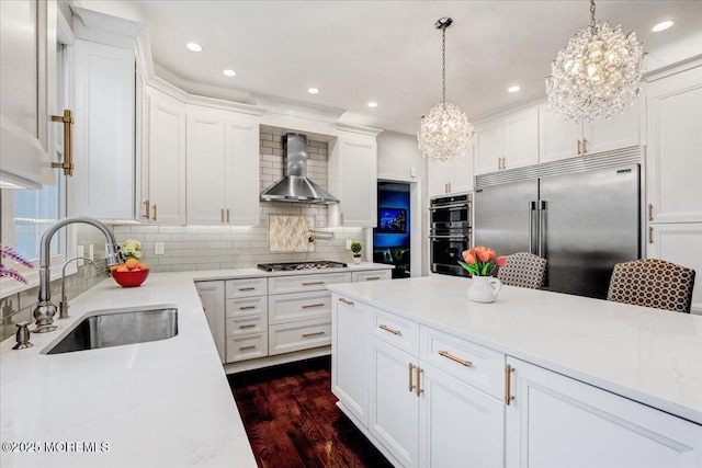 kitchen featuring a sink, wall chimney range hood, appliances with stainless steel finishes, a chandelier, and light countertops