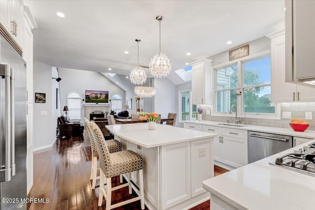 kitchen with stainless steel appliances, a sink, a center island, open floor plan, and dark wood-style flooring