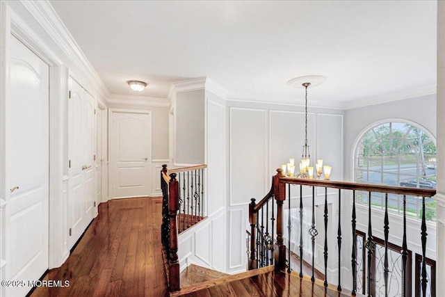 hallway with an upstairs landing, a decorative wall, a chandelier, dark wood-style flooring, and crown molding