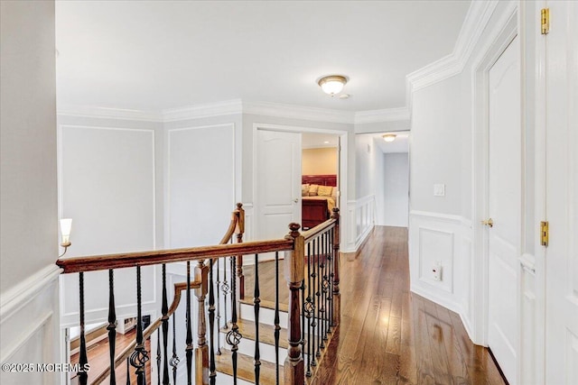 hallway featuring an upstairs landing, a decorative wall, wood finished floors, ornamental molding, and wainscoting